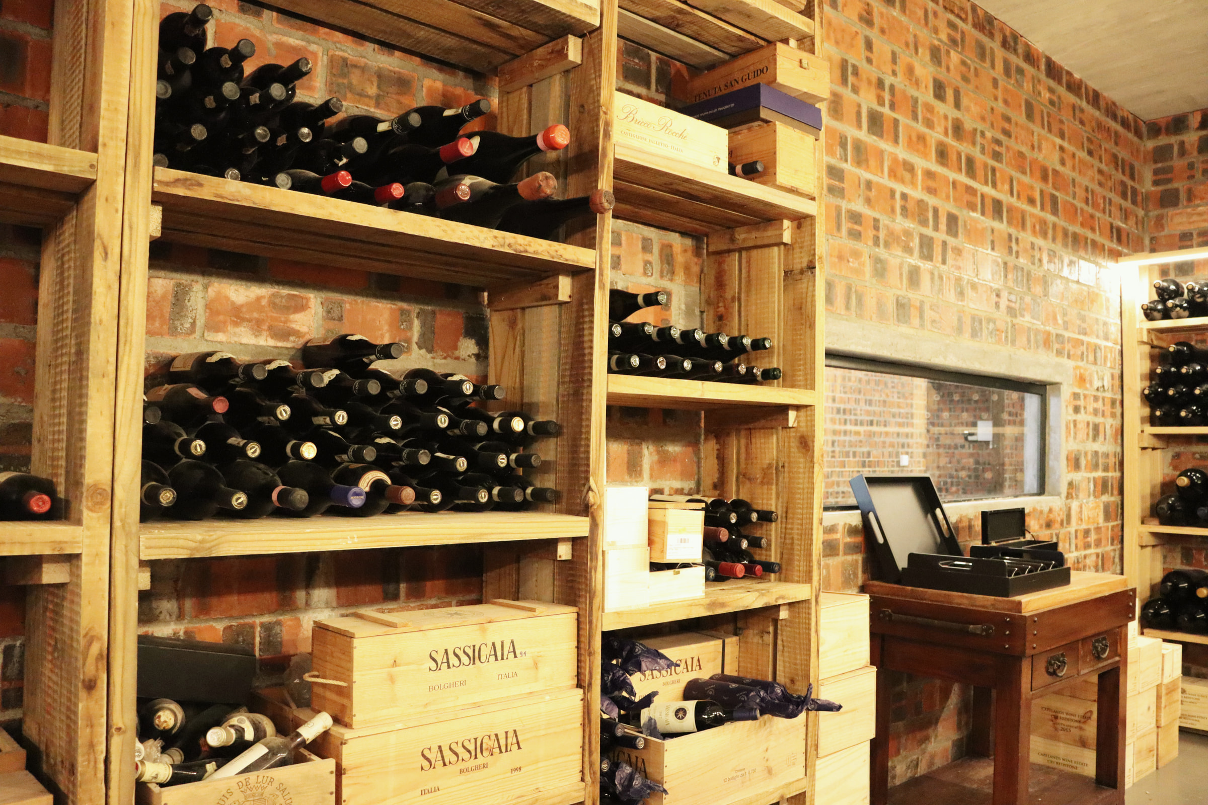 Wooden racks of wine bottles in the cellar, with Sassicaia cases stacked below against a brick wall