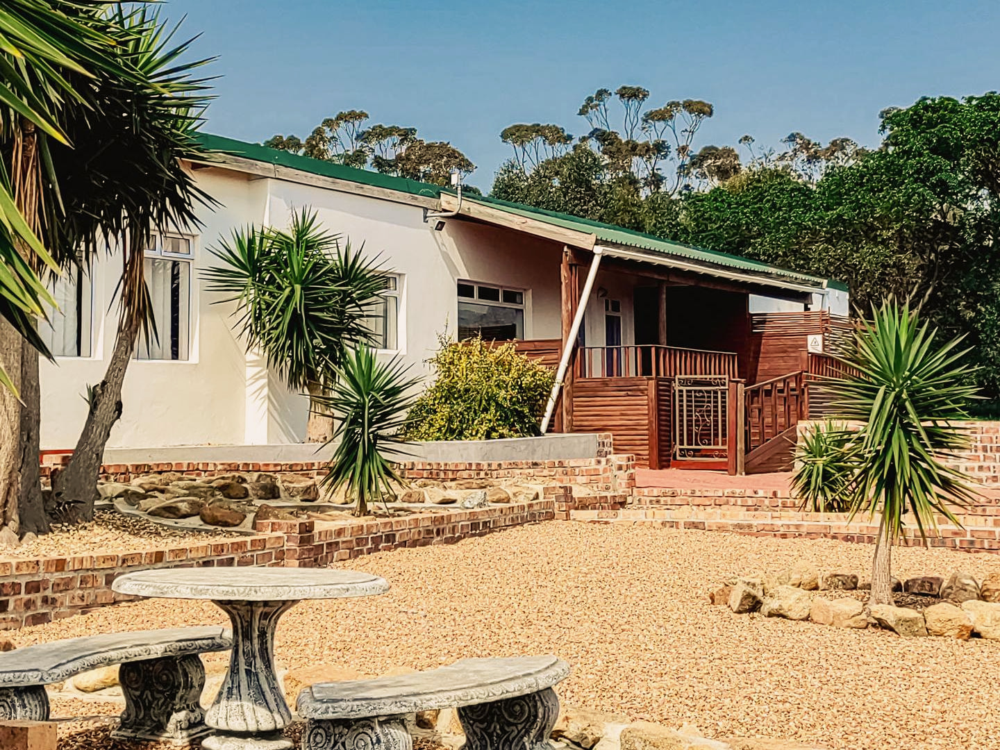 A whitewashed farmhouse with its timber deck, palms and a stone table